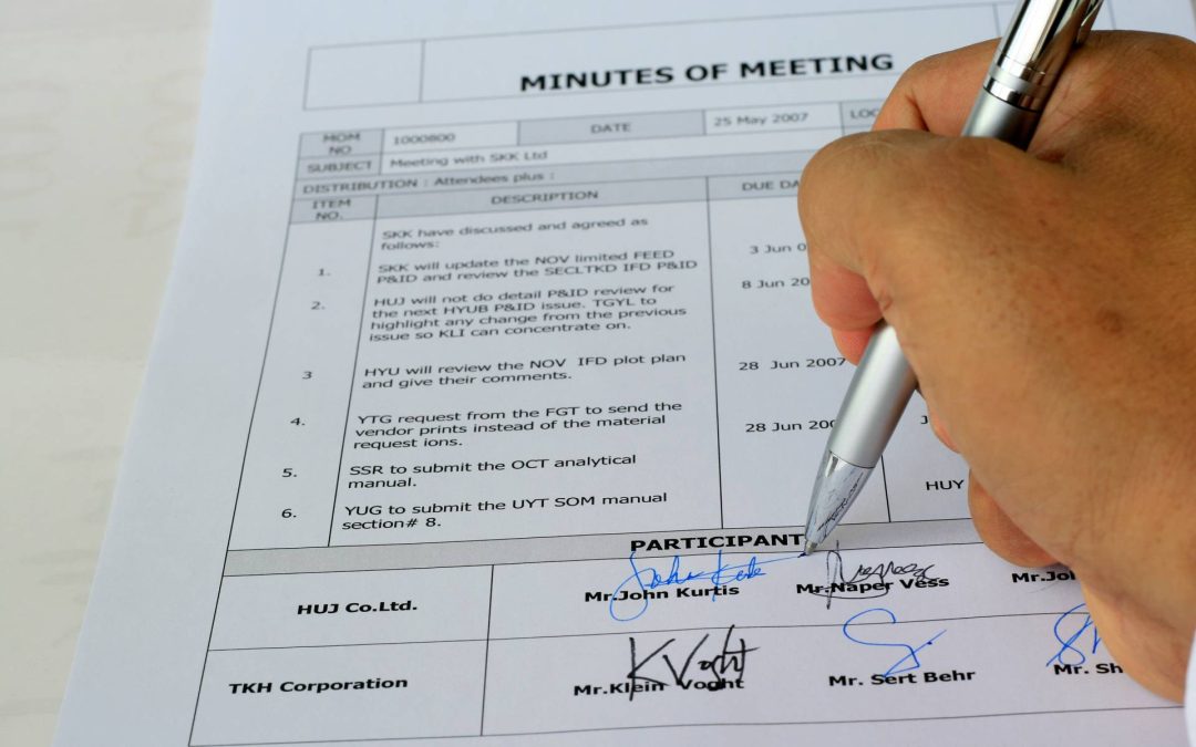 A hand holds a pen, then pen is being used to sign a generic meeting document.