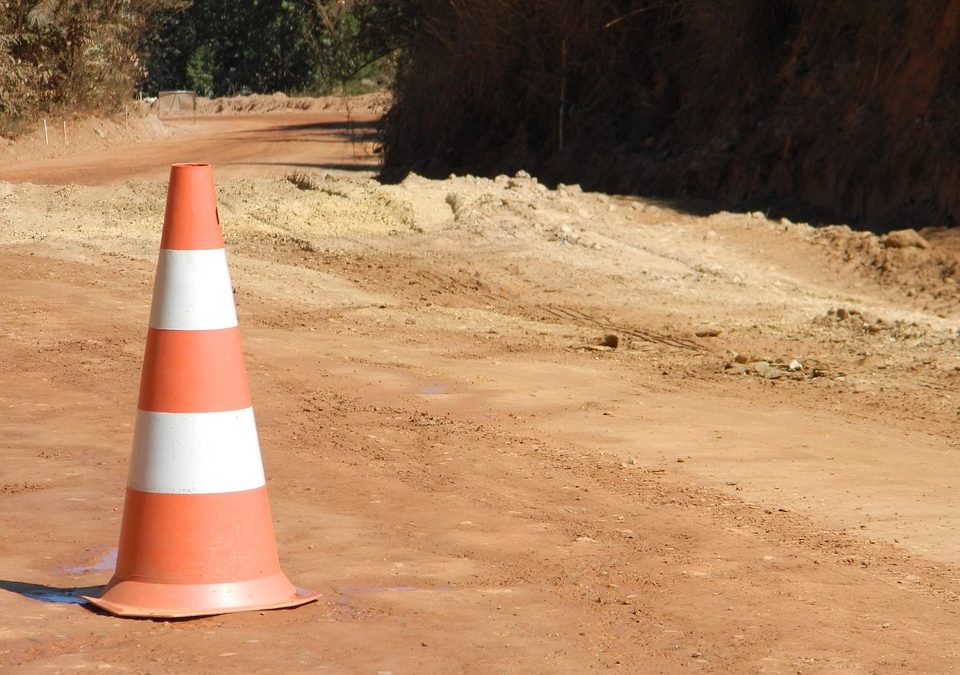 A striped traffic cone sits on a road.