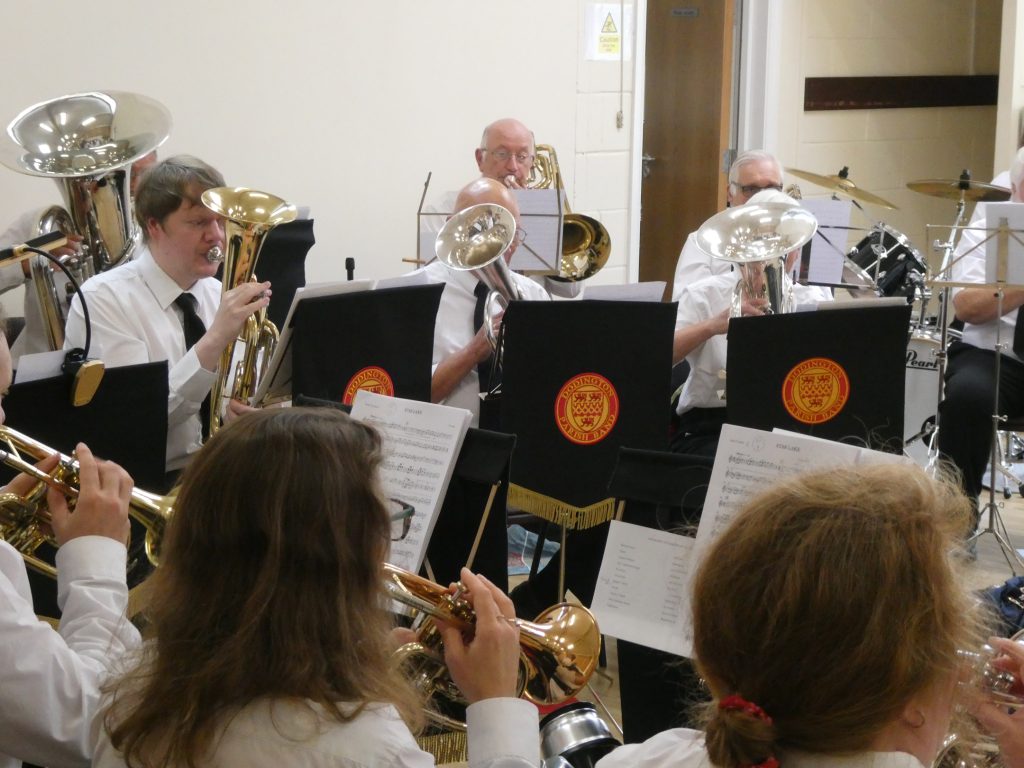 A group of musicians in uniform play a variety of brass instruments in a hall.
